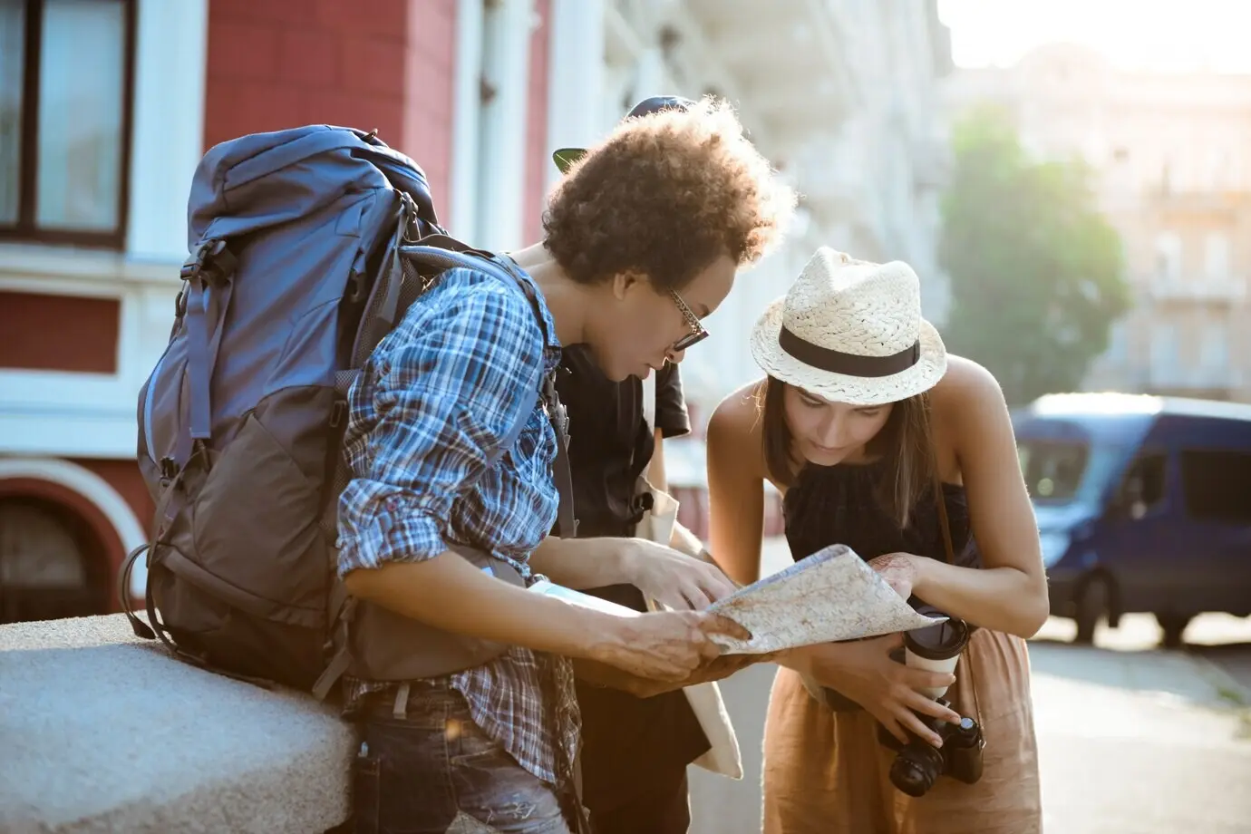 Друзья-путешественники с рюкзаками улыбаются, рассматривая маршрут на карте на улице.